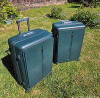 Two teal Bodysac spinner suitcases standing upright in yard