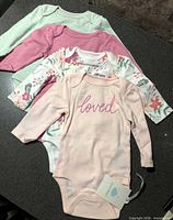 Four new Cloud Island long sleeve baby bodysuits arranged overlapping