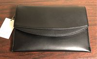 Front view of black clutch purse with tag attached