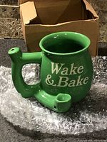 Green ceramic Wake & Bake mug with integrated pipe next to original box