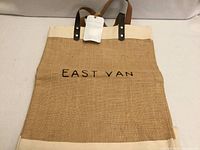Front view of burlap tote showing EAST VAN text and leather straps with tag