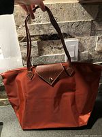 Tote bag opened showing rust nylon body, brown faux-leather flap and handles