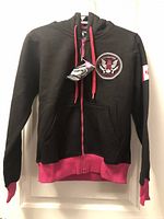 Full front view of hoodie showing color contrast, chest emblem, sleeve flag patch and attached retail tag