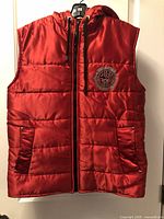 front view showing red quilted vest, zipper, hood, pockets and chest patch