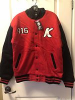 Front view of red and black varsity jacket hanging on door