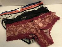 Stack of five underwear showing burgundy floral lace, black lace, grey leopard print, coral and purple pairs