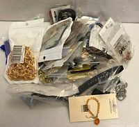 Pile of poly-bagged jewelry pieces, visible gold chain, packaged items, watch-style strap and beaded bracelet
