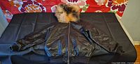 Front view of black leather bomber jacket with fur hood displayed flat