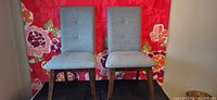 Full view of both gray-blue upholstered dining chairs in front of floral backdrop