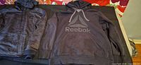 Under Armour and Reebok hoodies side by side on surface