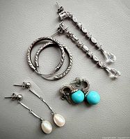 All four pairs of sterling silver earrings laid out on neutral background