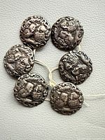 Six silver buttons arranged to show cherub design and size