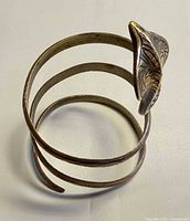Top view of coiled brass cobra armlet showing three loops and engraved patterns