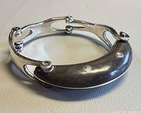 Side view of sterling silver hinged bracelet showing curved front segment with dot inlays.