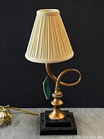 Lamp with shade in place showing brass body, decorative loop arm, black base