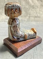 Front‐left view of glazed ceramic seated figurine on wood base