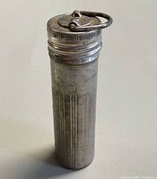 Closed metal match safe upright showing body grooves and lanyard loop on lid