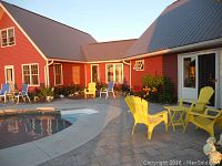 Red painted home with metal roof, in-ground pool with curved concrete deck and yellow Adirondack chairs