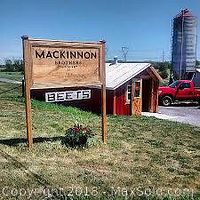 Outdoor view of Mackinnon Brothers Brewing Co. sign on bicentennial farm with red pickup truck and silo in background