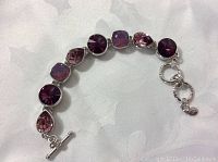 Close-up photo of the silver-tone bracelet adorned with multiple purple and pink Swarovski crystals in round, square, and teardrop shapes with toggle clasp.