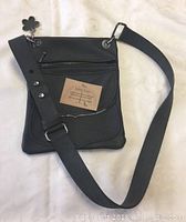 Full view of charcoal grey leather purse showing front side with zippered pocket and adjustable strap with flower charm.