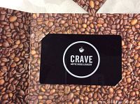 Close-up of a black gift certificate card with Crave Coffee House & Bakery logo on coffee bean-themed background.