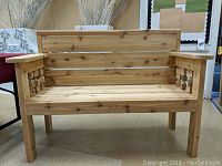 Front view of the unpainted cedar bench showing slatted seat, backrest and decorative cube armrests.