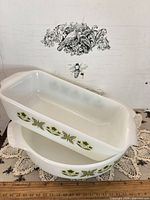 Rectangular dish resting on round dish, showing green floral band and milk glass material