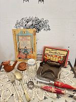 Overall view of all items in lot including booklets, utensils, shaker, cookie cutter, copper mold, pie vent