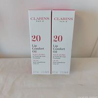 Front view of two boxed Clarins Lip Comfort Oil units