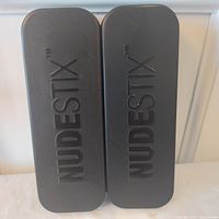 Two black Nudestix metal tins closed, embossed branding visible