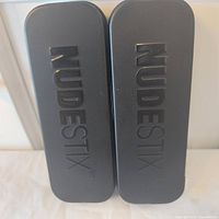 Two black NUDESTIX metal tins, closed