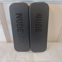 Front view of two black NudeStix tins