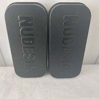 Two closed black metal NudeStix tins side by side
