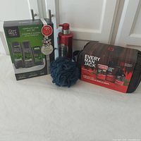 Group image showing all four items: Dove Men+Care gift box, Old Spice bottle, mesh puff, Every Man Jack gift pack with toiletry bag