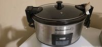 Front view of Elite Gourmet stainless steel slow cooker showing brand badge, locking lid mechanism, and overall exterior