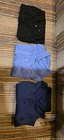 Folded view of black, light blue and navy polo shirts