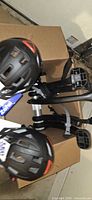 Top view of two black Zefal helmets with tags and portions of bike rack inside cardboard box