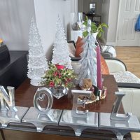 Overall view of silver NOEL stocking holders, clear acrylic trees, silver glitter tree, floral arrangement, candle holder with candle, teddy bear figurine