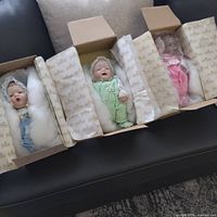 Three baby dolls in open boxes showing outfits and packing
