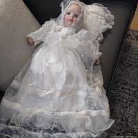 Full view of porcelain christening doll in white gown and bonnet