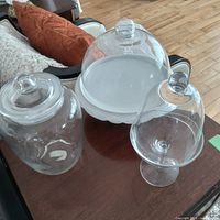 All three glass pieces grouped on tabletop: cake plate with dome, cylindrical jar with lid, footed candy jar with dome