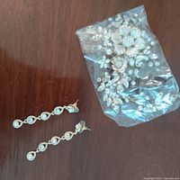 Hairpiece in plastic bag alongside drop earrings on wooden surface