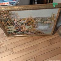 Framed needlepoint artwork leaning against furniture