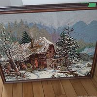 Front view of framed needlepoint winter cottage scene