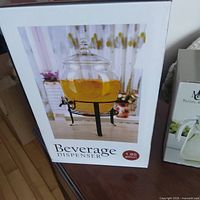 Boxed beverage dispenser showing image, capacity label 1.85 gallons