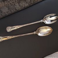 Two Italian silver serving spoons on black surface