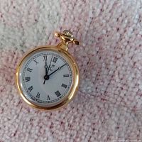 Round gold-tone pendant watch with Roman numerals on white dial
