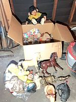 Overview of box and contents on floor: visible plush monkey, box of mixed toys, plastic horses, gnome figurines, metal sleigh