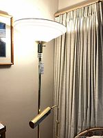 Tall brass torchiere floor lamp lit, showing uplight bowl and side reading arm